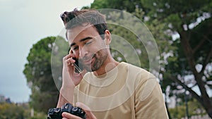 Joyful photographer speaking mobile phone in park close up. Man looking photo