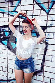 Joyful pin-up girl is posing next to a painted brick wall