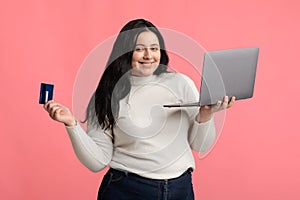 Joyful Plump Woman With Laptop And Credit Card Over Pink Background