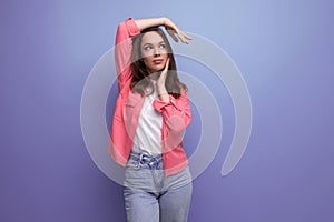joyful positive brunette young woman with shoulder-length hair in a pink shirt and jeans isolated on a plain background