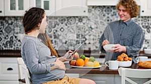 Joyful pregnant woman with dreadlocks drinks tea and watching her curly husband cooking breakfast for her in kitchen