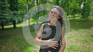 Joyful pregnant woman talking looking at camera standing on sunny green park meadow. Portrait of cheerful happy