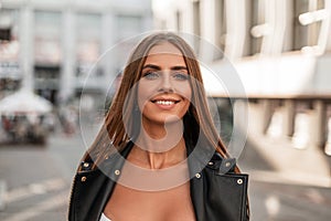 Joyful pretty young woman with blue eyes with brown hair with a lovely smile in a fashionable black leather jacket enjoys a walk