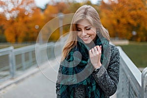 Joyful pretty young woman in a vintage autumn stylish coat in a fashionable checkered scarf standing on the street