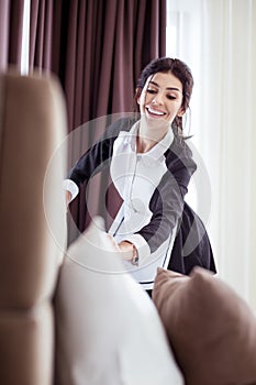 Joyful professional hotel maid cleaning the room