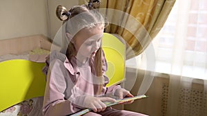 Joyful reads a book sitting on pull-out furniture with a beautiful face girl lighter in a children`s room in fashionable