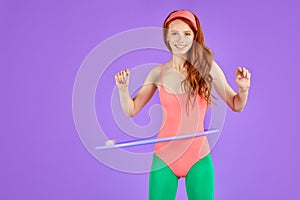 Joyful red-haired slim girl rotates hula hoop