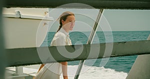 Joyful relaxed woman in a summer outfit leans on a boat railing with vast ocean view on the background. Water activities