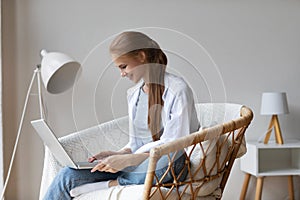 Joyful relaxed woman using laptop with interest sitting on a chair at home