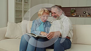 Joyful retired couple watching family photo album and sharing happy memories