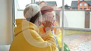 Joyful Reunion of Two Women Meeting Through Window with Colorful Background in Modern Home Setting