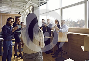Joyful satisfied business people applauding their female colleague at team meeting in office.