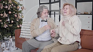 Joyful senior Caucasian couple chatting and laughing on Christmas at home. Portrait of cheerful husband and wife sitting
