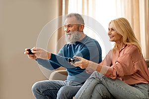 Joyful senior couple holding joysticks playing video games at home