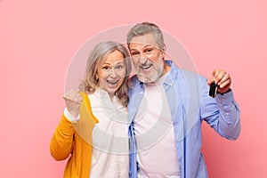 Joyful senior couple holding new car keys gesturing yes, studio