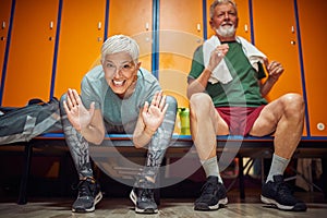 Joyful senior couple sitting in gym locker room, feeling energized and acting goofy, pre workout