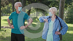 Joyful senior couple training in park in coronavirus face masks smiling touching elbows in slow motion. Caucasian man