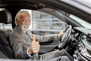 Joyful senior gentleman giving a thumbs-up while driving a sleek car