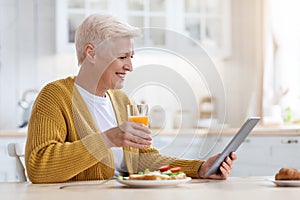 Joyful senior lady with digital tablet having lunch, side view