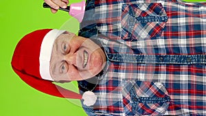 Joyful senior man in Santa hat rings Christmas jingle bell and laughs.