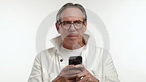 Joyful Senior Man Texting on Smartphone in Youthful Jacket on White Background