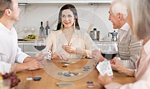 Joyful senior parents and young couple sitting around table playing poker