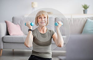 Joyful senior woman exercising with dumbbells to online video tutorial at home
