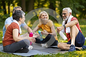 Joyful senior yoga enthusiasts enjoying friendly chat while sitting on mats outdoors