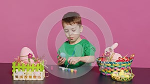 Joyful small kid painting eggs for easter holiday festivity in studio photo