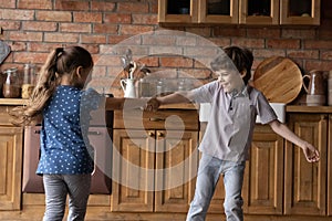 Joyful small kids siblings dancing spinning around kitchen holding hands