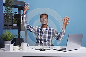 Joyful smiling african american office worker happily lifting hands in air because of successful business plan.
