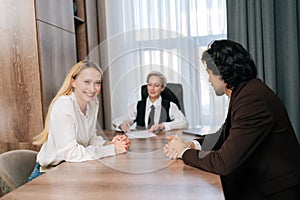 Joyful smiling business people having conversation sitting at desk in conference room, gathered for project discussion