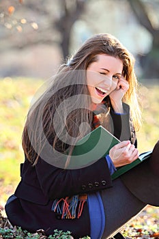 Joyful and smiling girl reading a book in the park