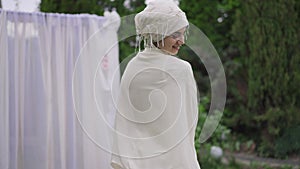 Joyful smiling Middle Eastern bride in white wedding dress and hijab spinning in summer garden at wedding altar