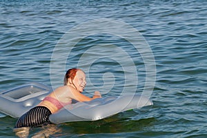 Joyful smiling teenage girl bathes with air mattress in the sea