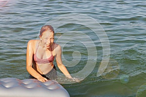 Joyful smiling teenage girl bathes with air mattress in the sea
