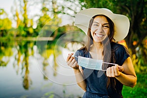 Joyful smiling woman holding hygienic mask in nature. Protected woman. End of coronavirus pandemic concept.Woman celebrating