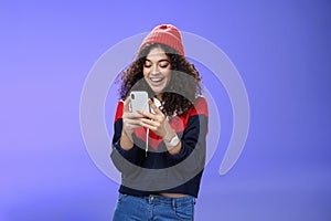 Joyful and sociable stylish caucasian woman with curls in warm beanie having fun laughing and chuckling as using