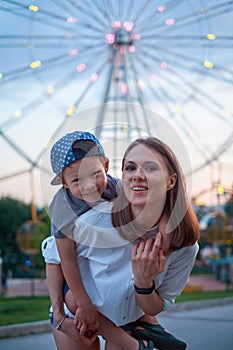 Joyful son hugs mom while walking in the park against the background of a ferris wheel.