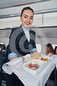 Joyful stewardess rolling airline meal trolley through aisle