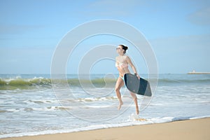 Joyful surfer girl happy cheerful going surfing at ocean beach running into water. Female bikini woman heading for waves