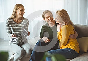 Joyful surrogate expectant mother showing ultrasound picture to couple