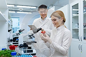 Joyful team of two people man and woman in white medical coats lab workers research food vegetables and fruits