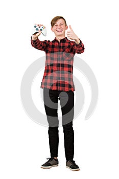 Joyful teen gamer showing his console joystick isolated over white background. Adolescent boy keeps thumb up positive gesture as