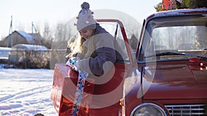 Joyful teen girl holding big gift box with red ribbon inside car on Christmas eve. Happy girl taking New Year present