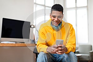 Joyful teen guy browsing smartphone with headphones