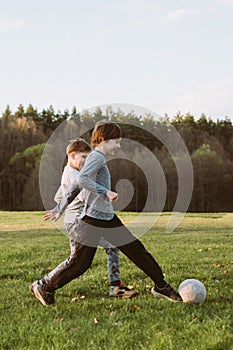 Joyful teen kicking ball while friend running close, active players practicing on lawn with happy expressions on faces.