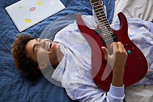 Joyful teenage guy laughing while playing electric guitar