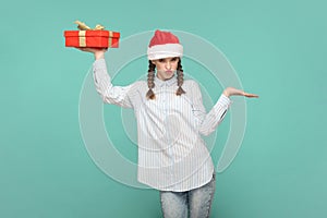 Joyful teenager girl in and Santa Claus hat, holding present box, presenting copy space on palm