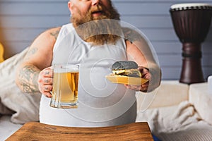 Joyful thick guy drinking alcohol with hamburger